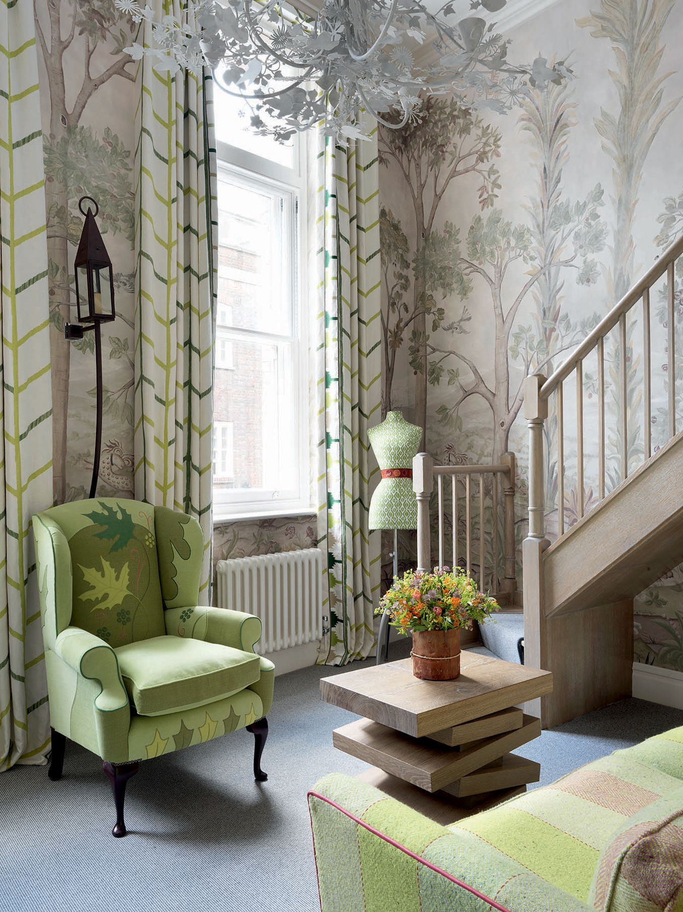 Sitting room interior space with tree patterned wallpaper, a green armchair, dress form, and couch