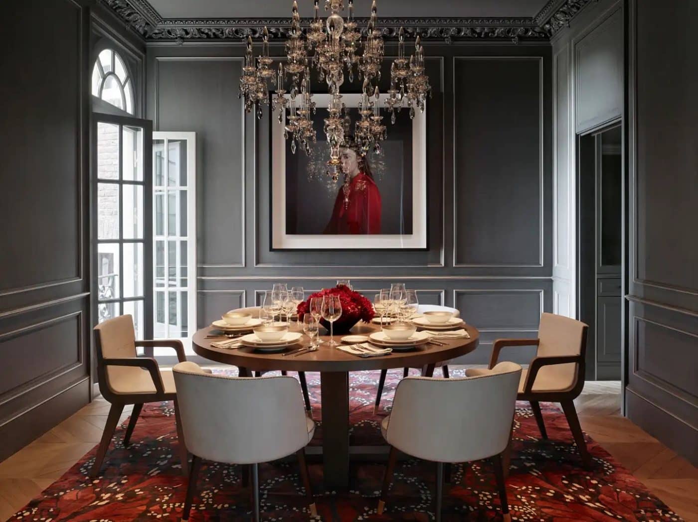 A a dove-gray San Francisco dining room by JKA design with a German crystal chandelier, a portrait of a figure wearing red by British photographer Richard Learoyd, a B&B Italia table, B&B Italia chairs and a red monarch-butterfly-patterned carpet by Alexander McQueen for The Rug Company
