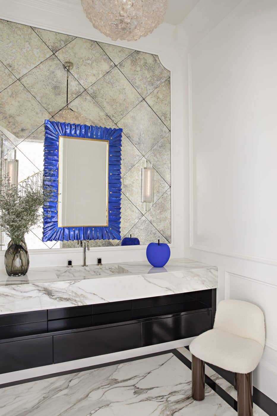 A vibrant blue mirror and velvet apple sculpture by Andrew Martin add a shock of color to a powder room