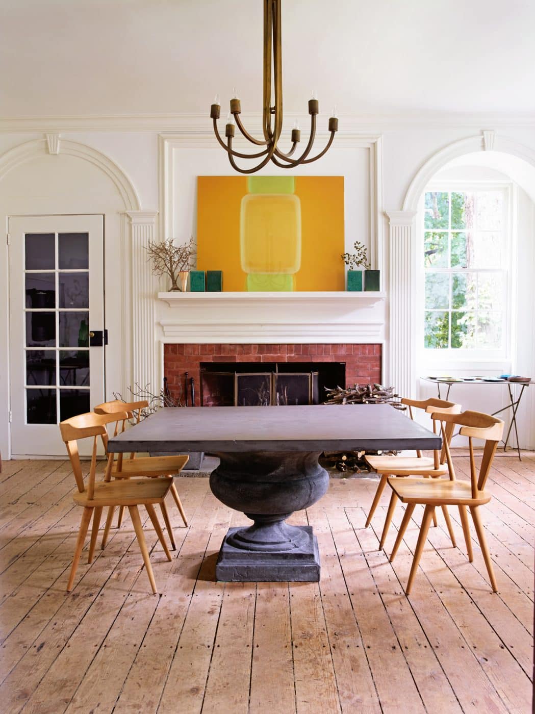 In the dining room of the Upstate New York home of architect David Mann and his partner, Fritz Karch, Paul McCobb chairs surround a classical-influenced cast-concrete and resin table; a photograph of Tupperware by Richard Caldicott hangs over the fireplace.