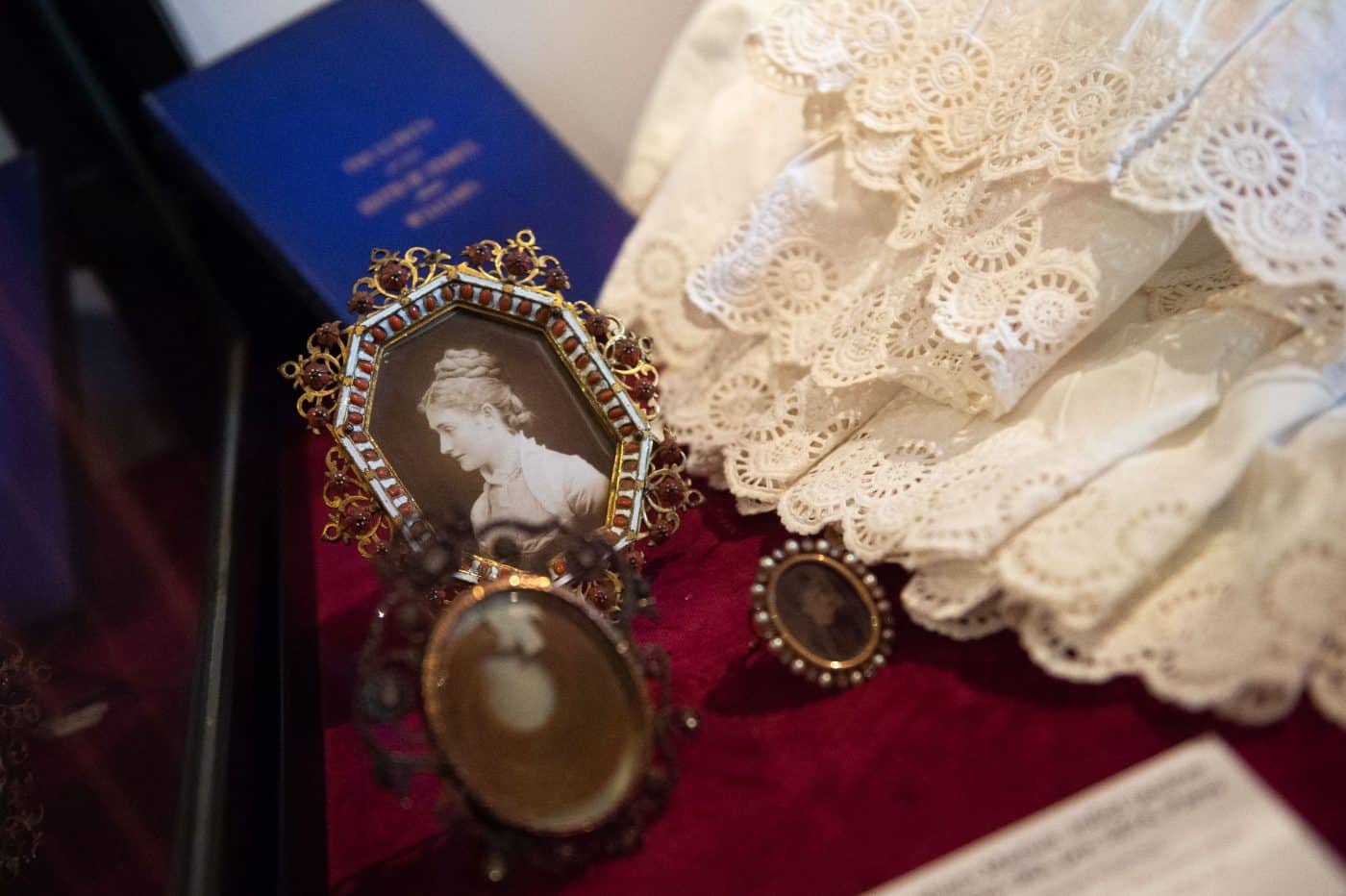 Small framed black-and-white family photos, lace and a blue-covered estate book in the Family Room at Waddesdon Manor part of the show "Alice's Wonderlands" about Alice de Rothschild in England