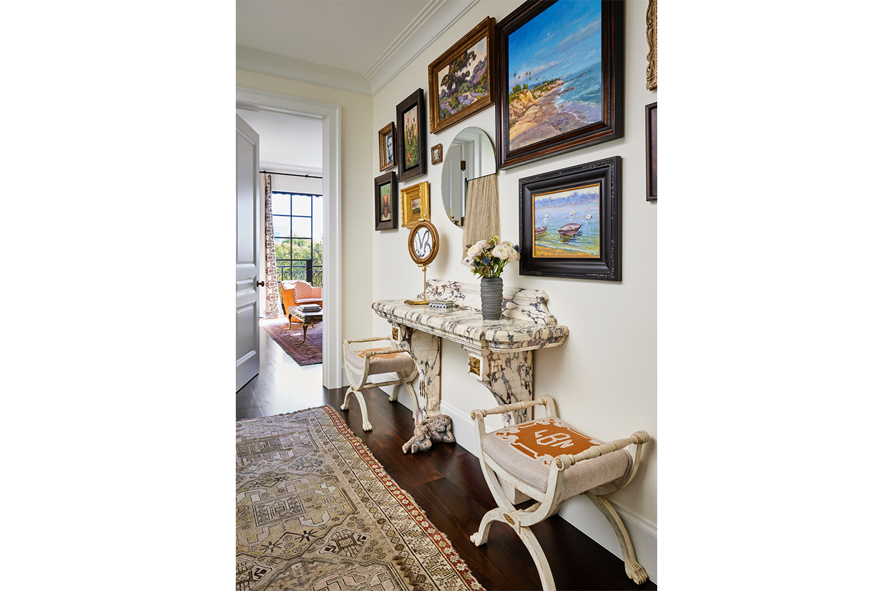 A hallway designed by Jeff Schlarb with a gallery wall and a marble mantel used as a console table