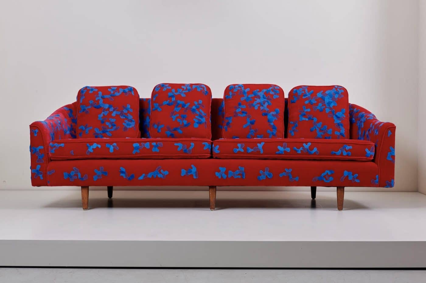 A large sofa with red upholstery custom embroidered with amorphous blue shapes