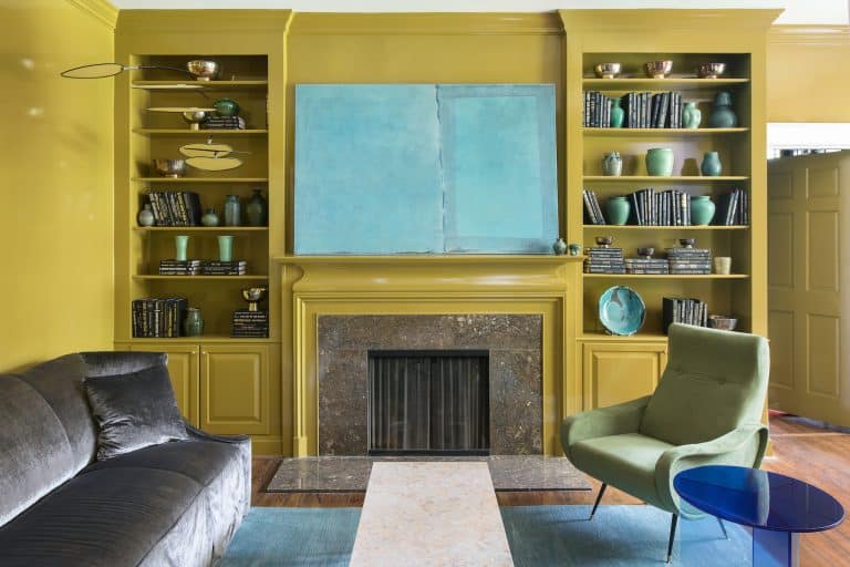 A living room designed by Jacob Laws with mustard-yellow lacquered walls and a large pale-turquoise painting over the fireplace