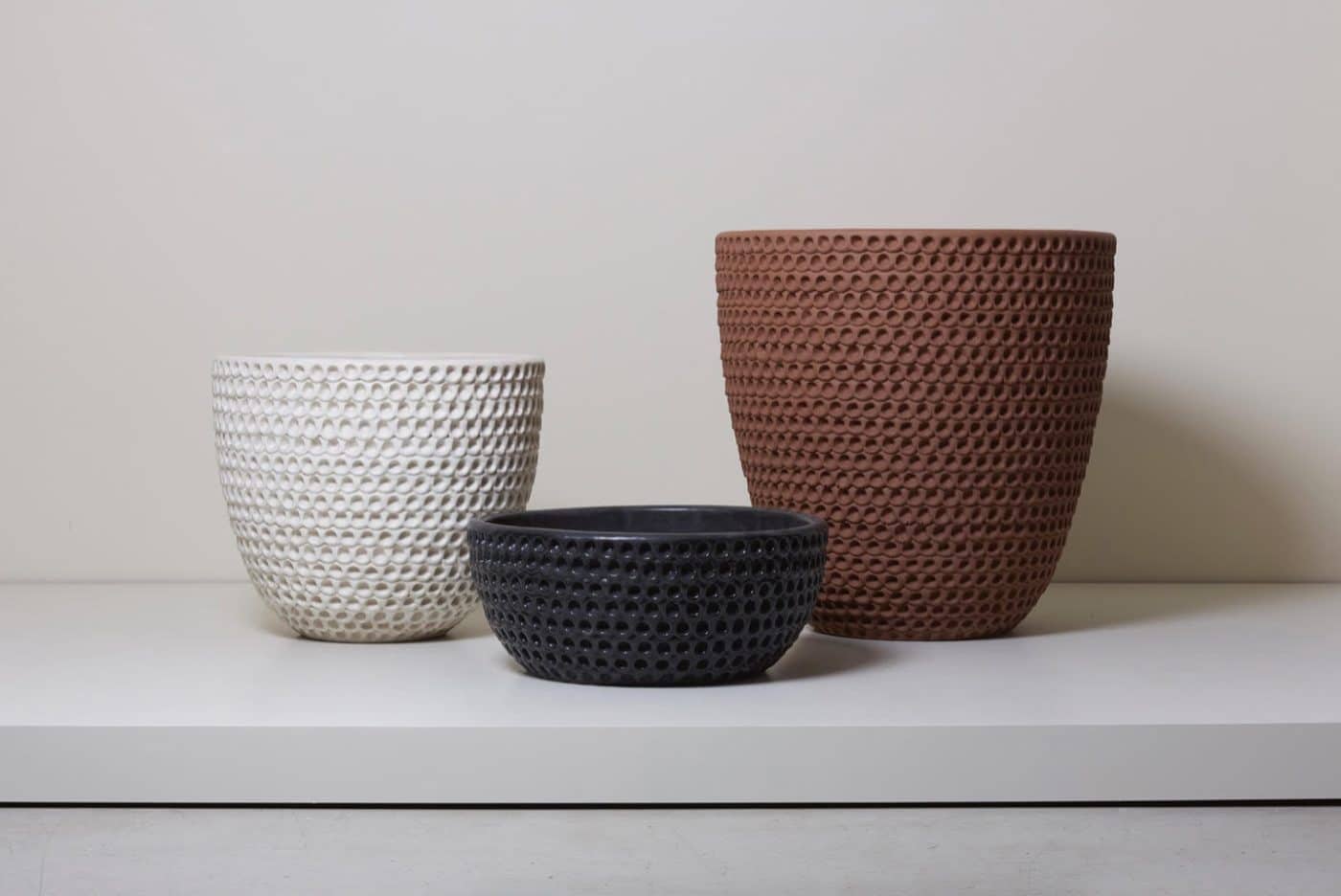 A trio of planters by Stan Bitters — one white, one black and one terra-cotta — textured with rows of circular imprints