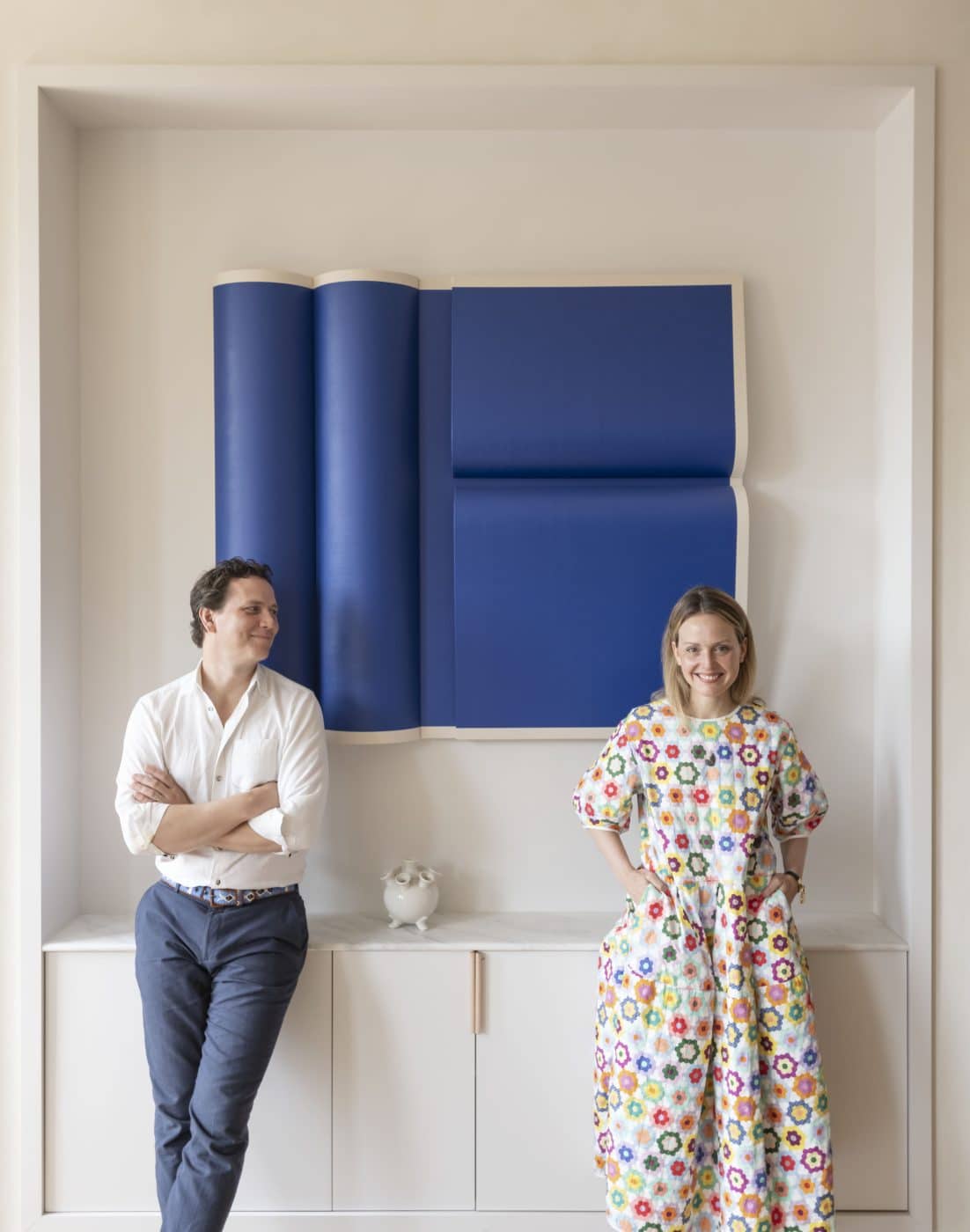 husband-and-wife designers Damian and Britt Zunino of Studio DB stand in front of a blue Robert Moreland painting in their New York studio
