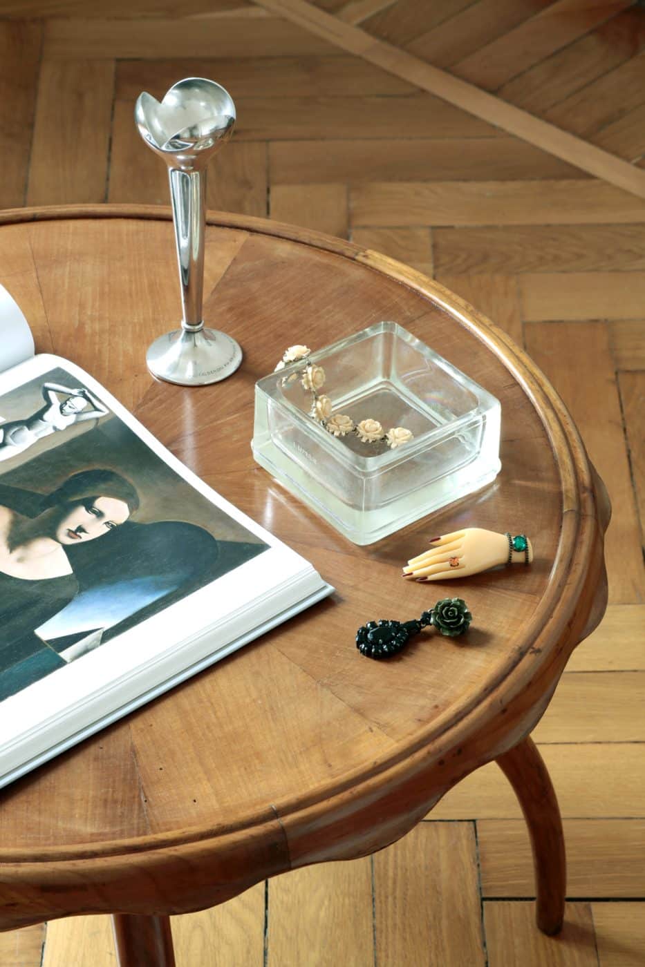 An Osvaldo Borsani cocktail table in Jenny Walton's Milan apartment with an open art book, a slender silver-plate vase, a square clear glass ashtray and vintage jewelry on it