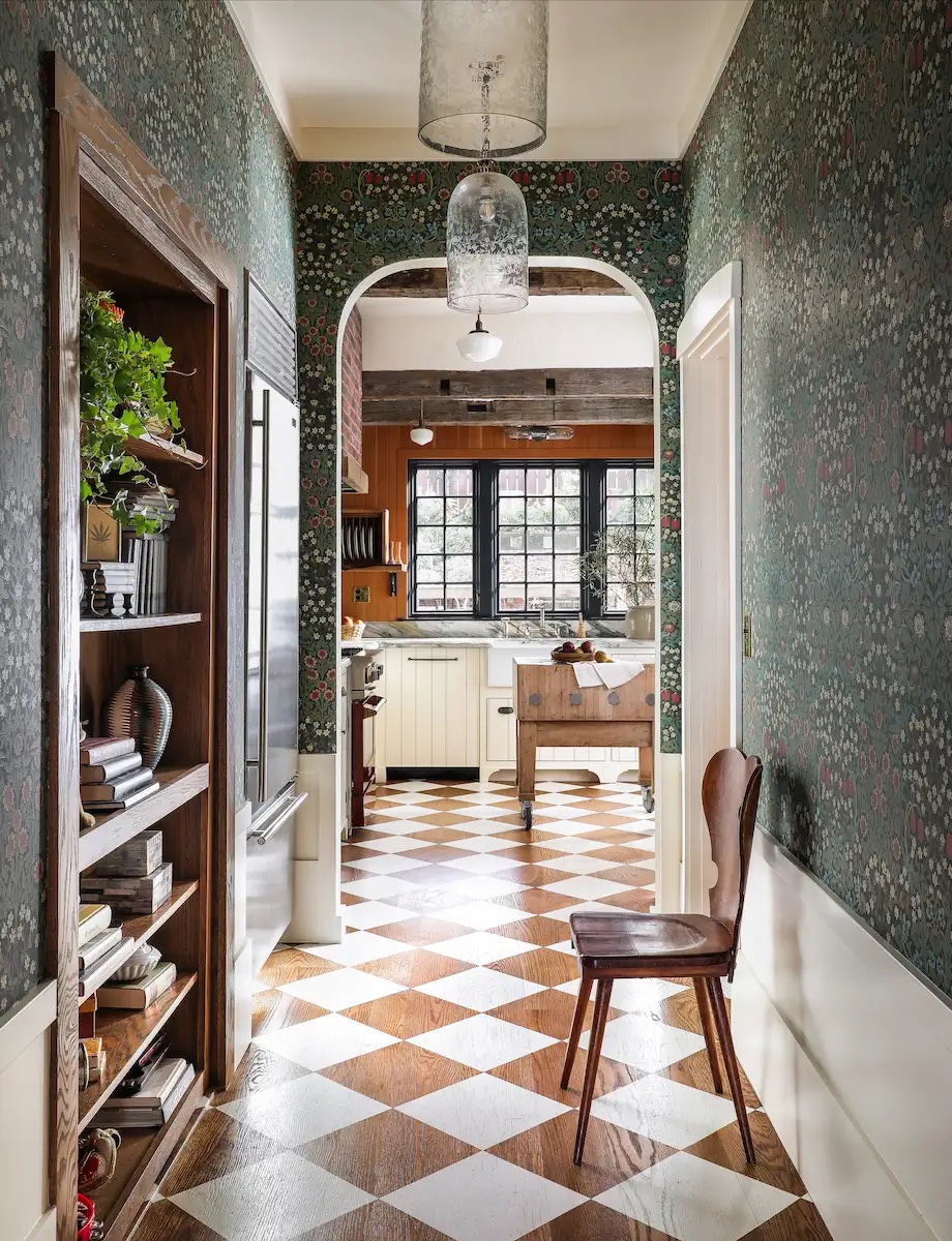 The hallway of an Arts & Crafts–style house, with a dark-green floral wallpaper and a brown-and-white checkerboard floor
