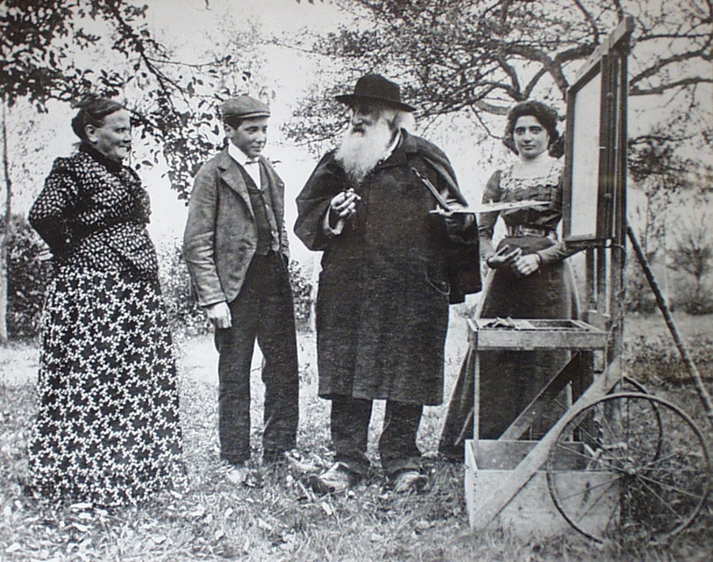 A black-and-white photo of Impressionist painter CAMILLE PISSARRO in a field in Éragny, France, with his wife, Julie, and his children PAULE-ÉMILE and Jeanne.