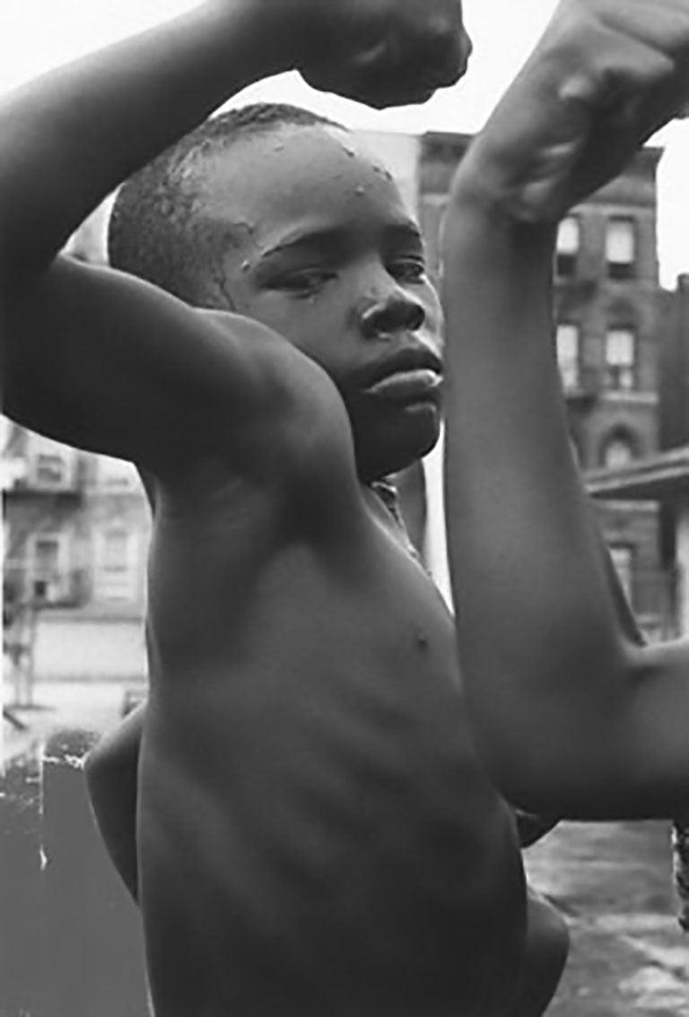 A black-and-white photo of an African-American boy flexing his muscle
