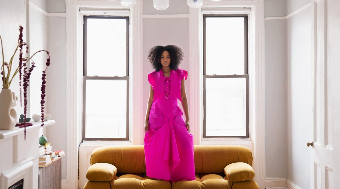Naomi Elizée wearing a fuchsia dress by Christopher John Rogers in the living room of her Brooklyn apartment