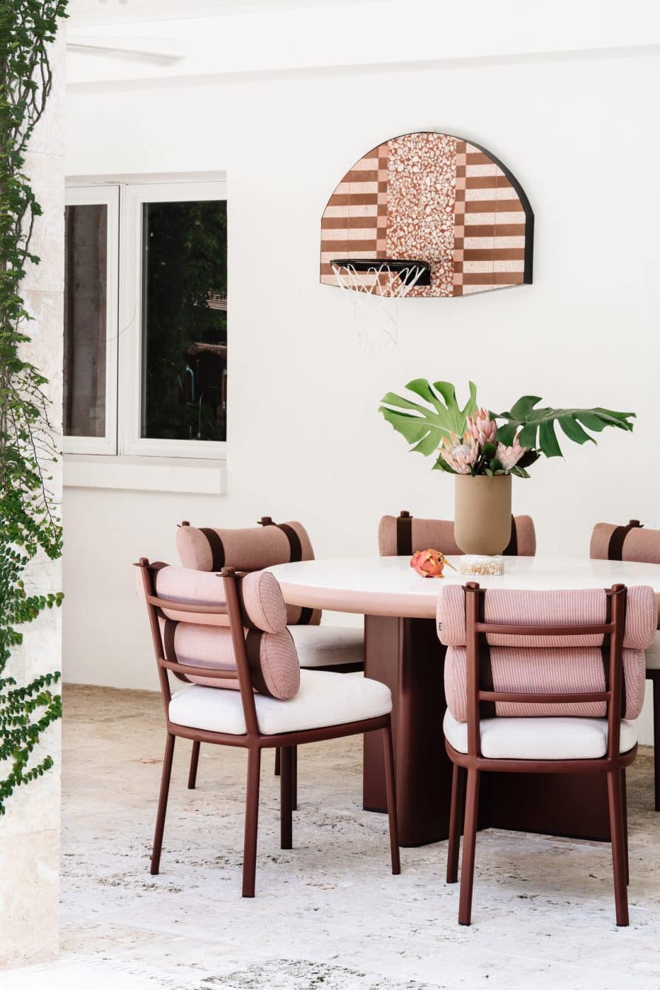 Miami interior design studio Moniomi's Lux Mini Hoop basketball hoop and backboard hangs on a wall behind a dining table and chairs
