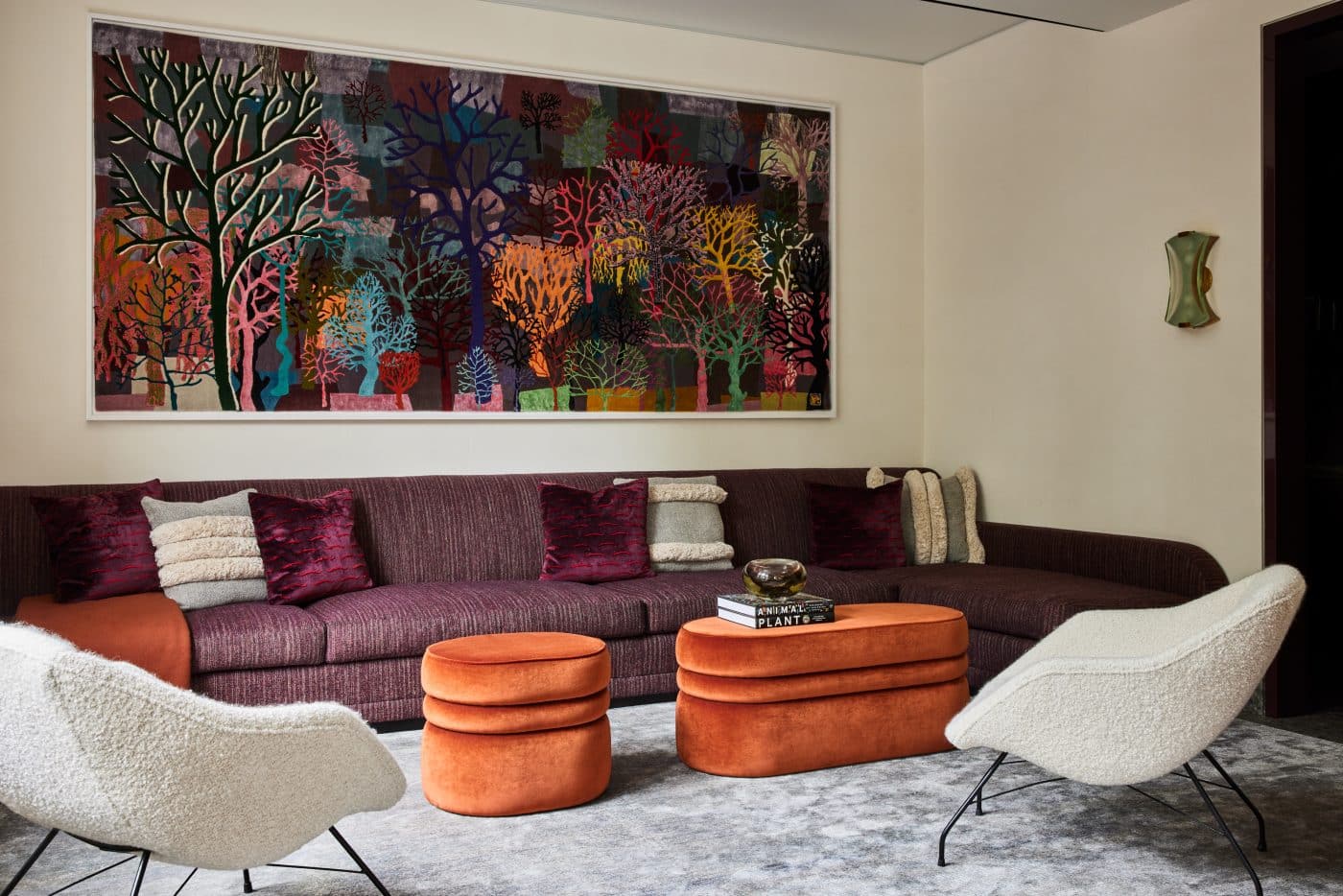 The den is furnished with bespoke pieces, including a plush sectional sofa in burgundy, plus a pair of orange velvet ottomans. Trenton Doyle Hancock’s tapestry Color Flash for Chat and Chew, Paris Texas in Seventy-Two, 2020, brings all the colors together.  