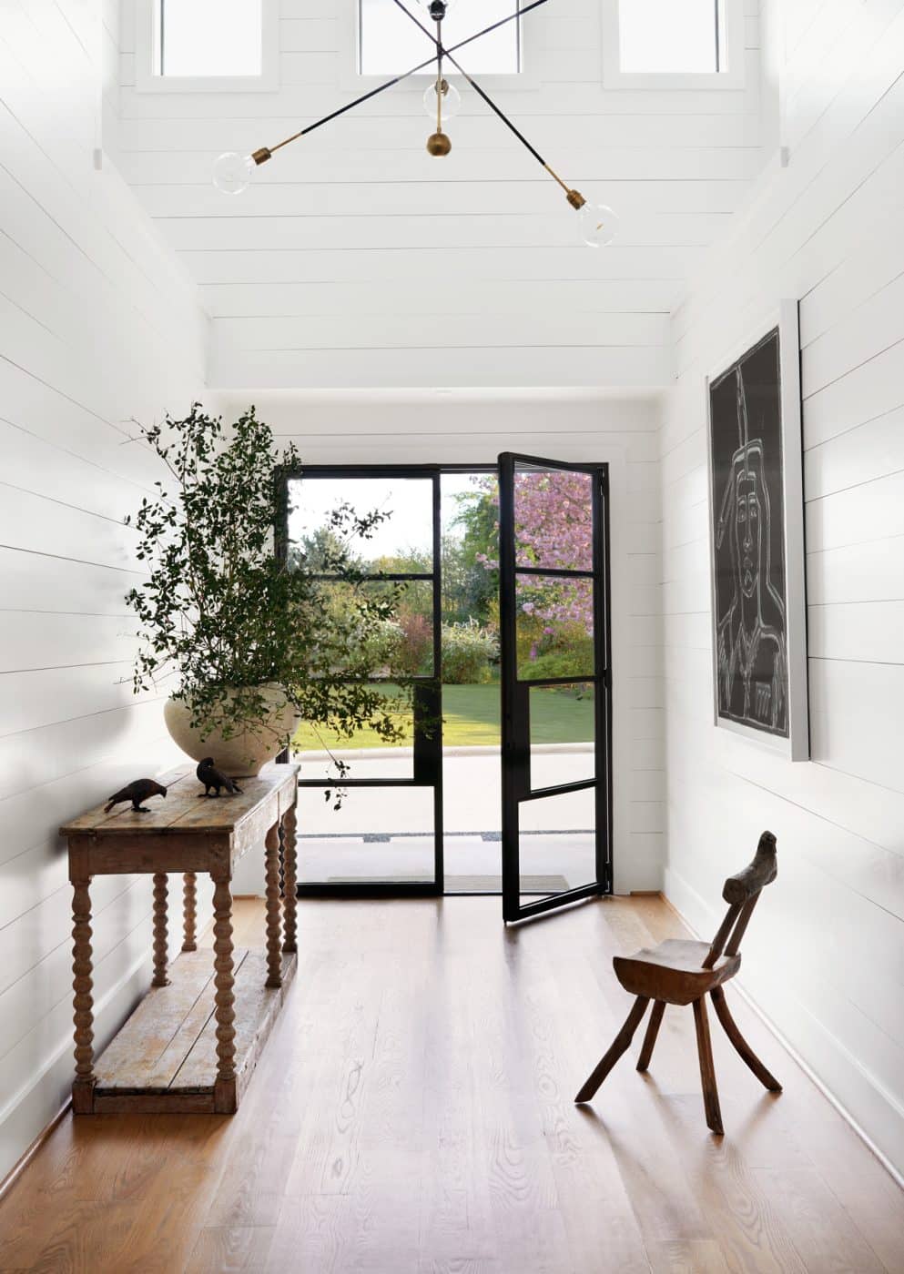 Back in the Hill Country home, this entry has a 19th-century French DRAPERY TABLE from 1stDibs via ALEXANDRA, art by AMERICA MARTIN and an APPARATUS Highwire Tandem chandelier.