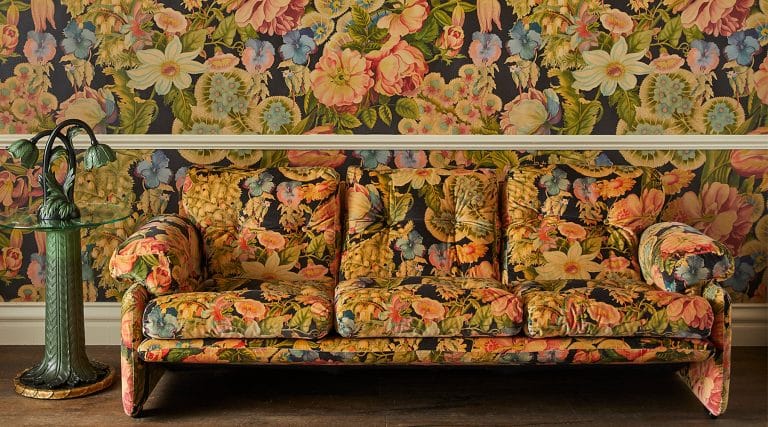 House of Hackney's Acanthus side table and table lamp next to a sofa covered in the brand's Amatoria print in front a wall papered with the same pattern