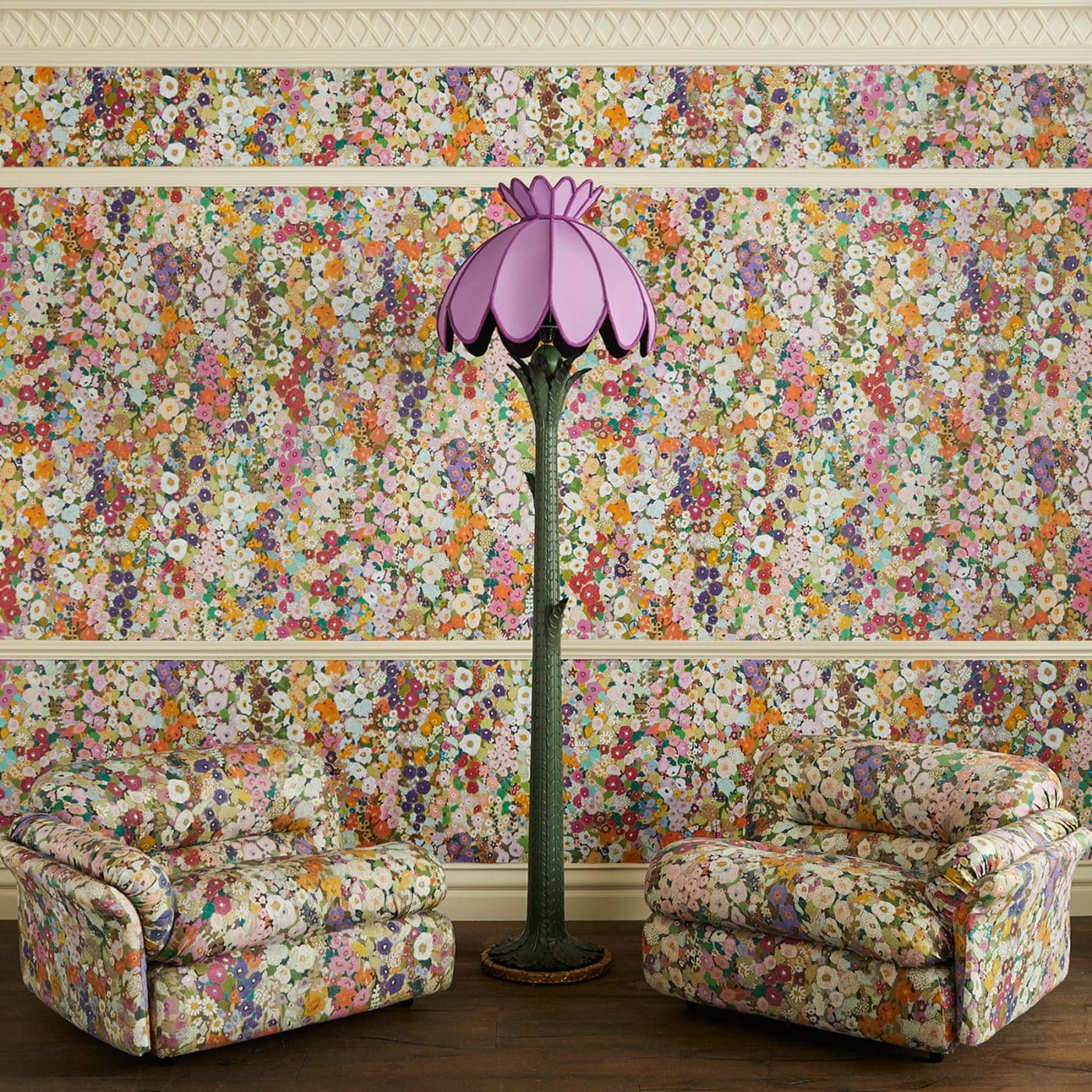 House of Hackney's green Acanthus floor lamp with a purple shade, flanked by two seats covered in the brand's Hollyhocks print in front a wall papered with the same pattern