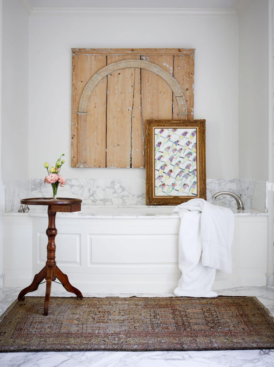 Around the bathtub are antiques in the form of a drinks table, rug and an architectural fragment on the wall. The aviary art is by Hunt Slonem.