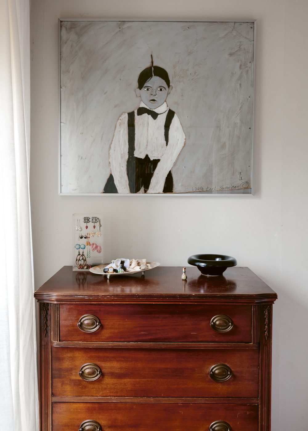 a view of  Camille Okhio’s Brooklyn apartment with a painting by Earl Swanigan and an antique dresser