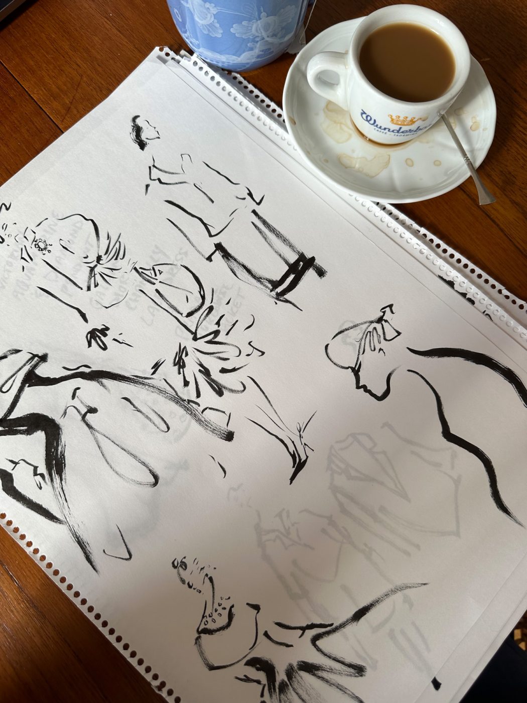 Pages of black-and-white sketches from Jenny Walton's notebook lying a wooden table next to a cup of coffee