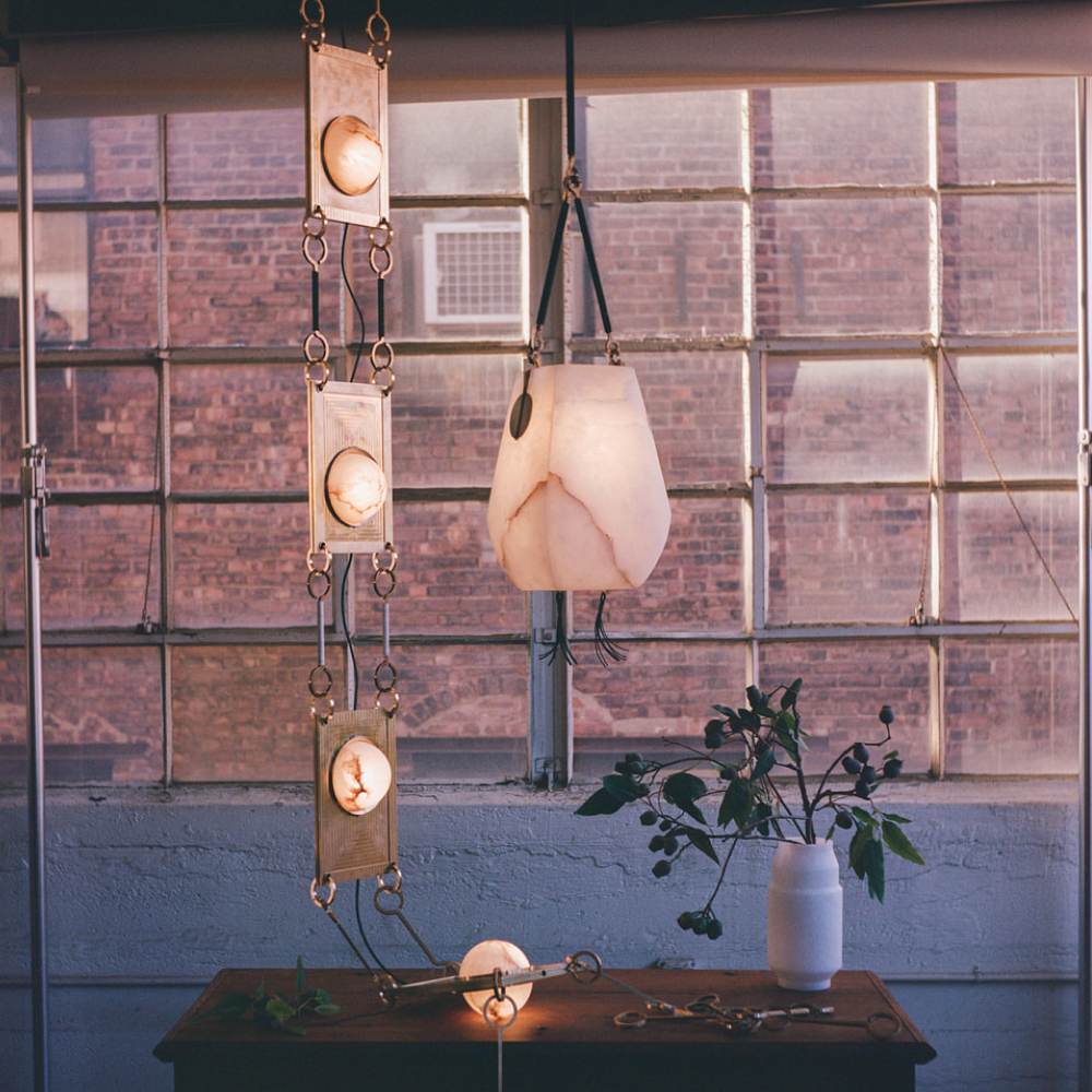 Matthew Fisher's Kalathi lantern and NIMA DROP CHANDELIER hang in front of a window at Remains Lighting Company's Brooklyn factory.