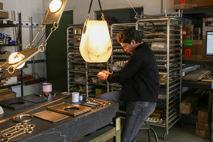 Matthew Fisher sits on a stool while working on a hanging lantern in the Remains Lighting Company's Brooklyn factory. 