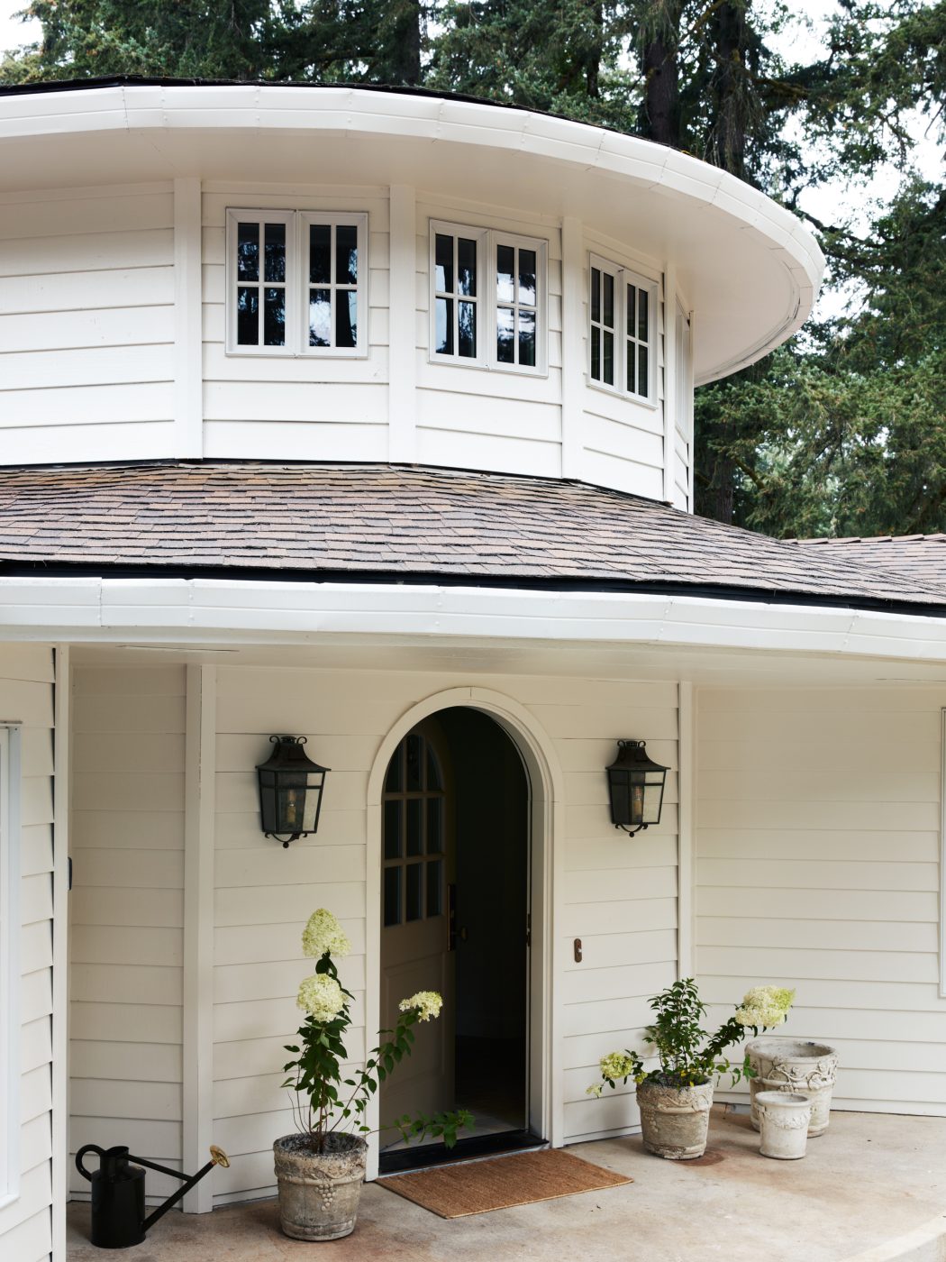 white clapboard exterior showing arched front door and silo-like double height entry of interior designer Molly Beth Kidd's Oregon home