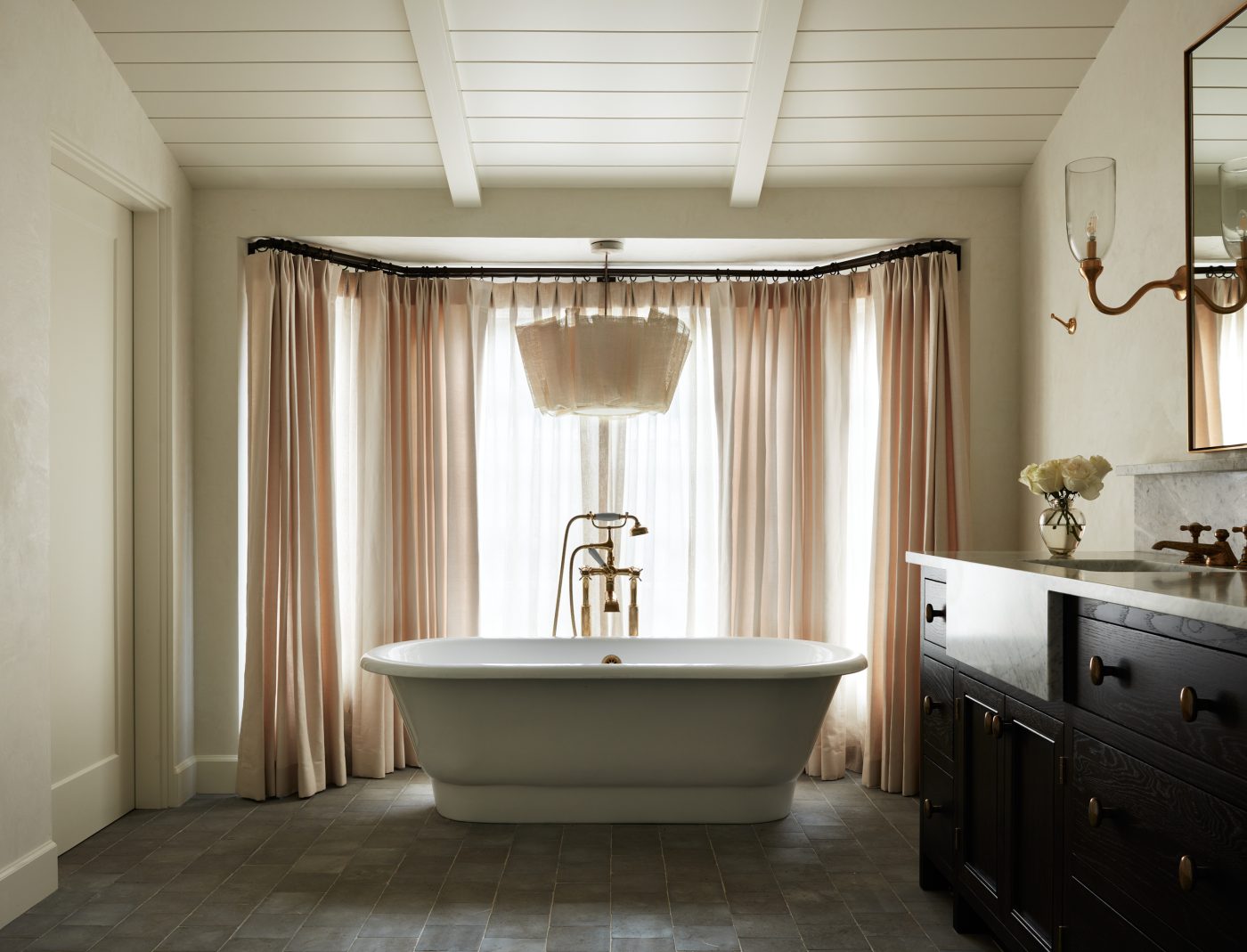 Freestanding soaking tub under gauzy pendant lamp in window bay in primary bathroom of interior designer Molly Beth Kidd's Oregon home