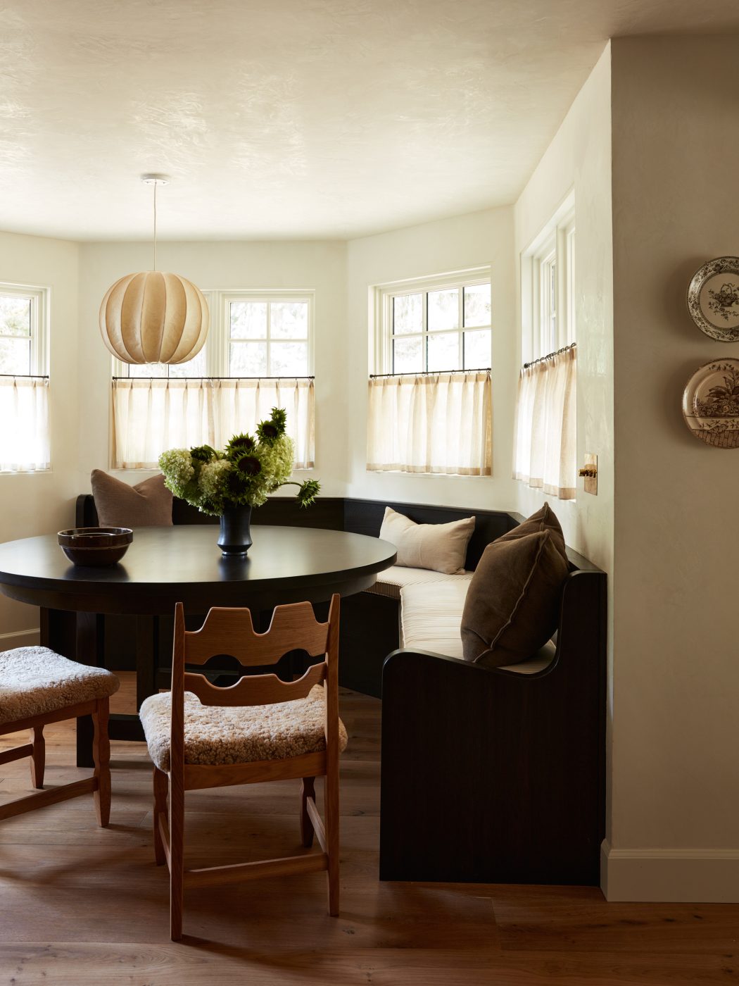 Breakfast nook banquette round table and wooden chairs under cocoon pendant light in kitchen of interior designer Molly Beth Kidd's Oregon home