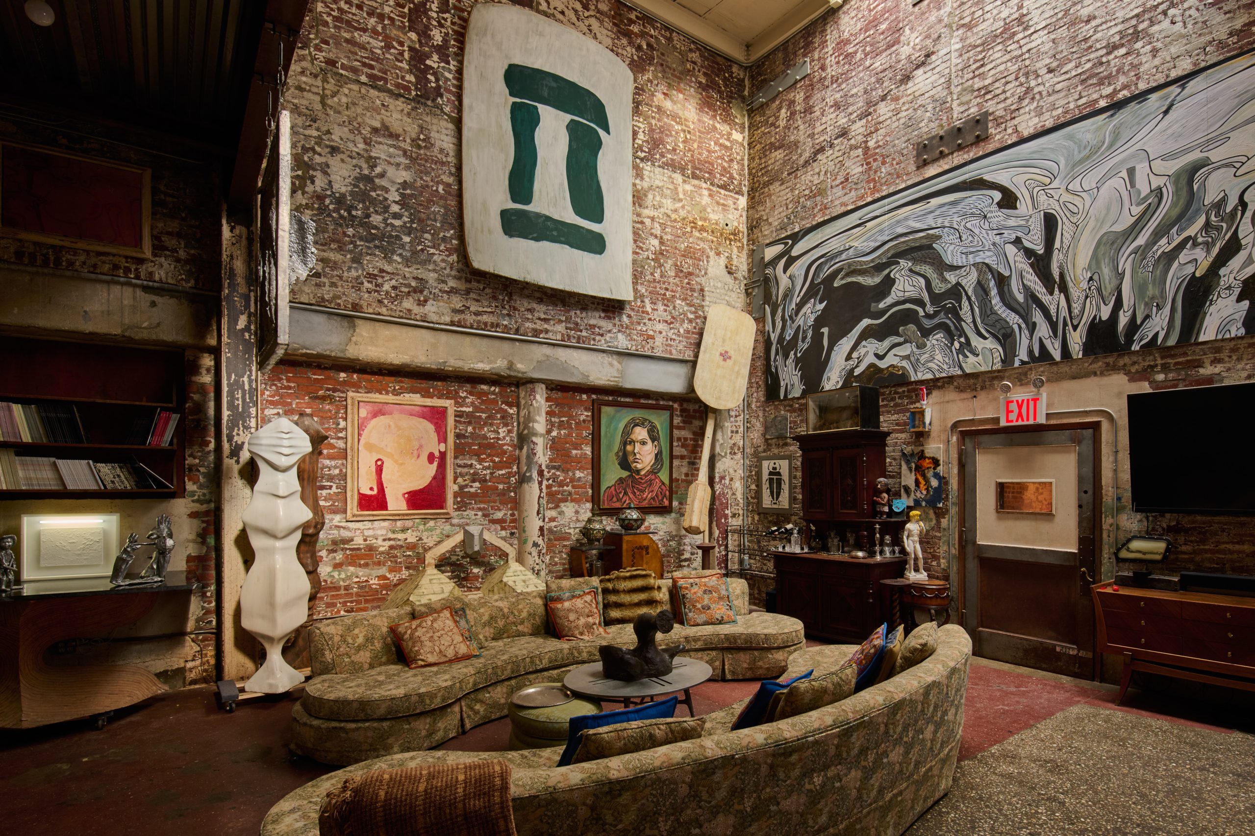 Living area of artist Ray Smith's home in his Brooklyn studio, fitted with two kidney shaped sofas and filled with art and objects