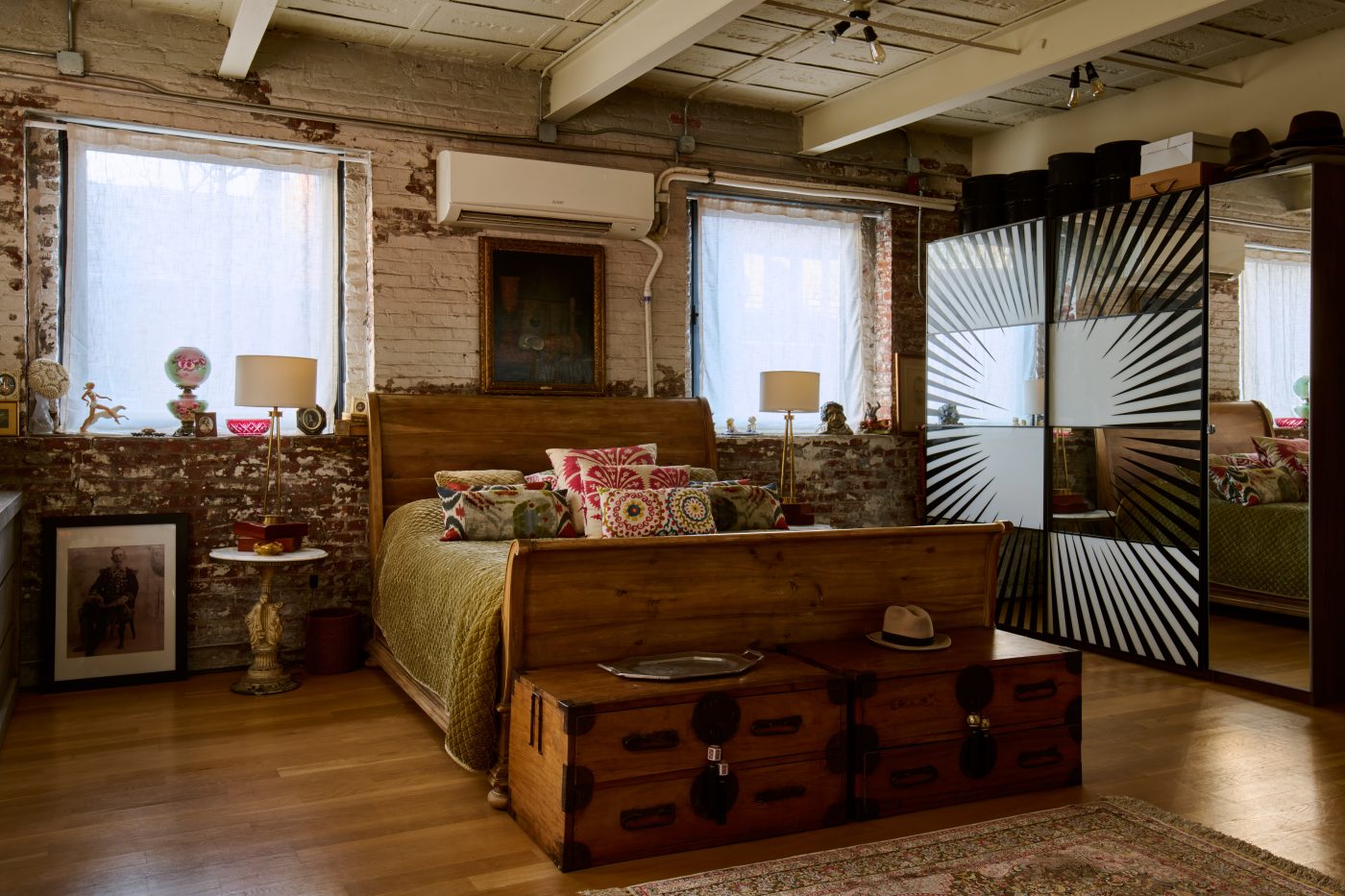 Bedroom fitted with sleigh bed and campagne chests at foot of bed and mirrored closet with starburst pattern in home of artist Ray Smith in part of his Brooklyn studio