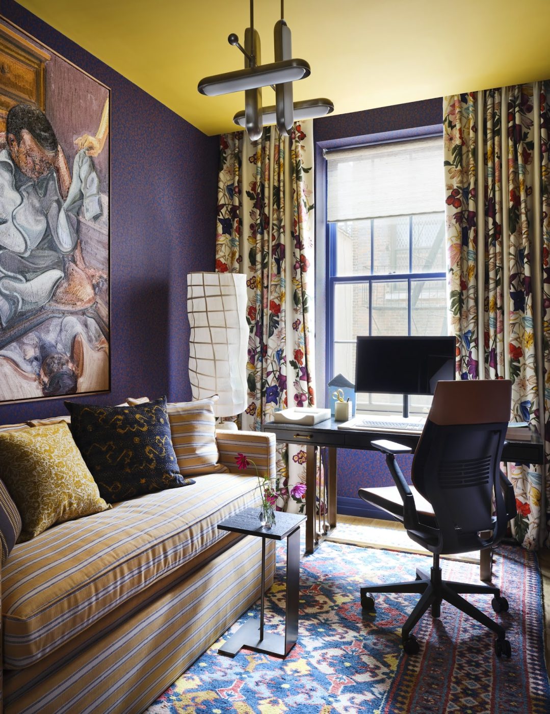 Rich color and pattern define the study, from its boldly patterned rug to its yellow ceiling. In between, a Dedar floral frames the windows, a Study in Tribeca loft designed by Kati Curtis with purple Zak + Fox covering swaths the walls, and a Timothy Lai artwork adorns the space over the sofa. The desk is by Julian Chichester, and the chair is STEELCASE.