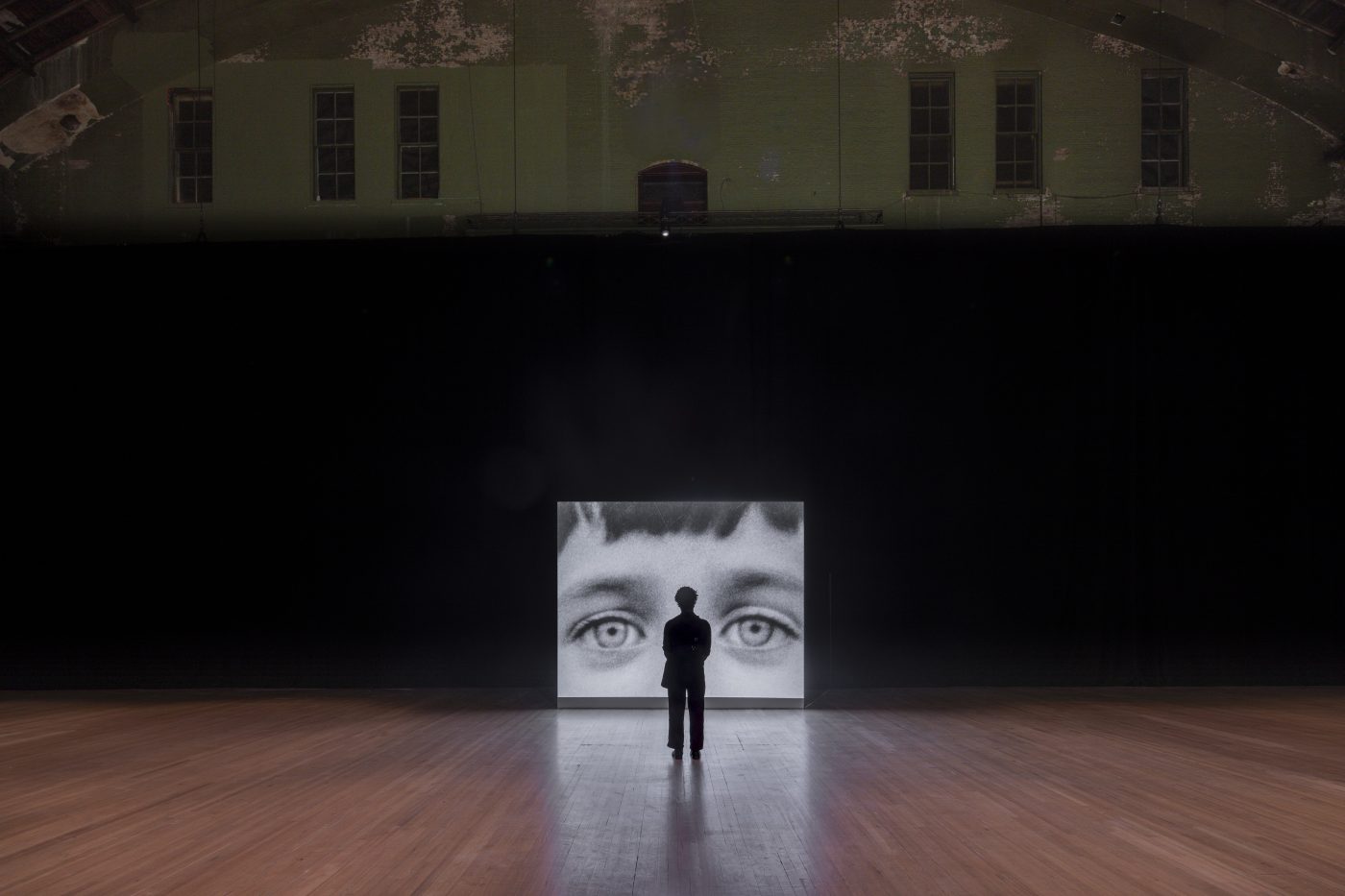 A photo of a person looking at a closeup of a Diane Arbus photograph projected onto a large screen at the Park Avenue Armory in New York City