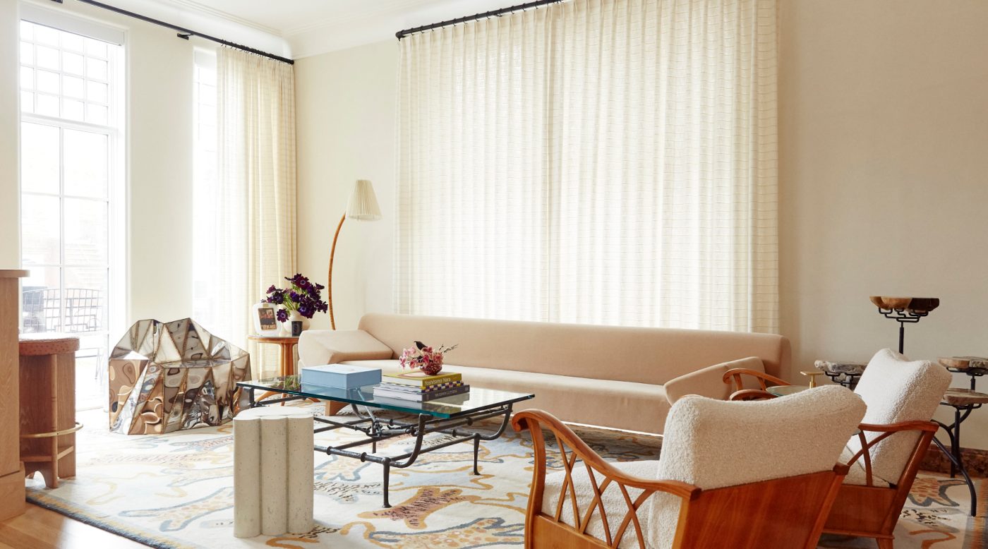 Living room with a long contemporary sofa, British artist Julian Mayor’s faceted mirror Glenda chair and a pair Maurizio Tempestini wooden-armed upholstered chair chairs on a Beauvais rug with a tiger motif, in a house in Brooklyn's Gravesend neighborhood with interior deisgn by Eli Dweck