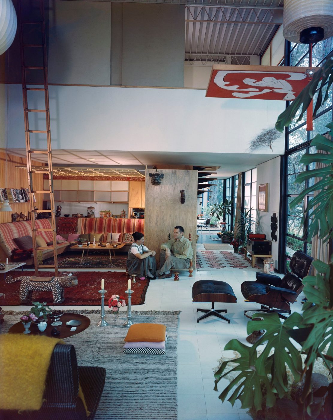 Designers Charles and Ray Eames sitting on low seating among colorful furnishings in their Los Angeles home