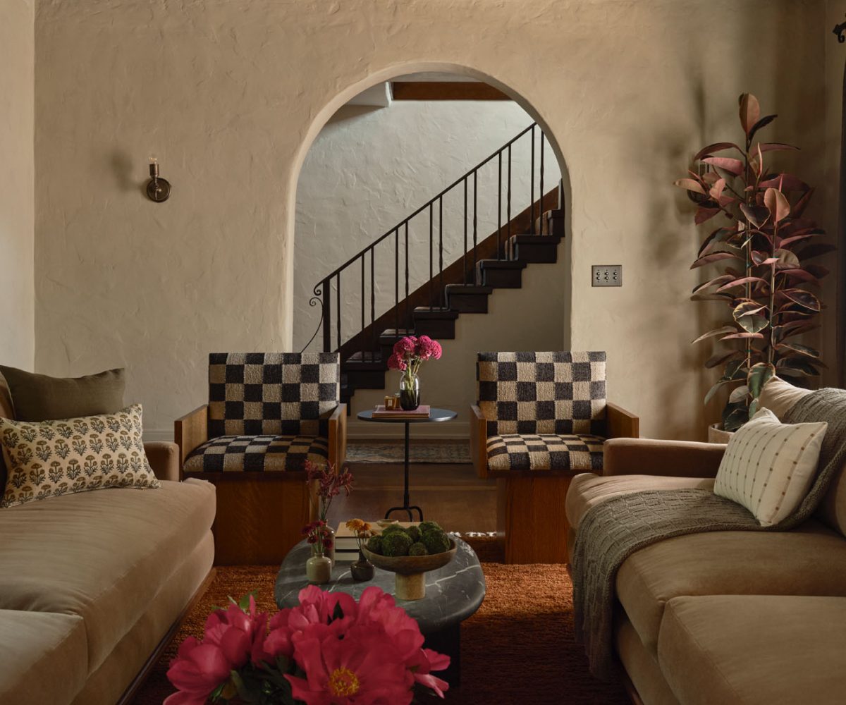 Living room with twin sofas flanking a series of marble coffee tables and pair of checkerboard print chair n front of arched opening to stairhall in Palo Alto Silicon Valley California Mediterranean house designed by Mandy Cheng
