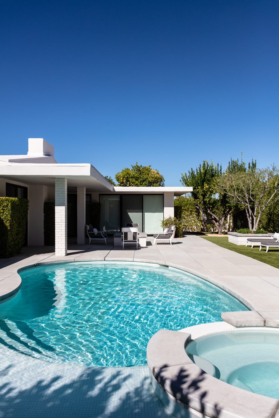 A classic desert modern house in Palm Spring California, low flat roof building all white behind kidney shaped pool. It is one of more than 250 that Du Bois designed for a residential enclave in Palm Springs.