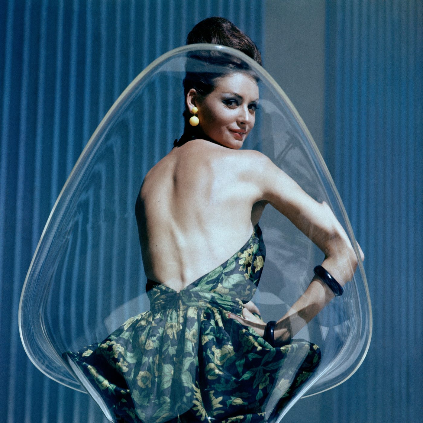Model Katherine Pastrie in a backless dress sitting in a transparent bucket chair designed by Estelle and Erwine Laverne