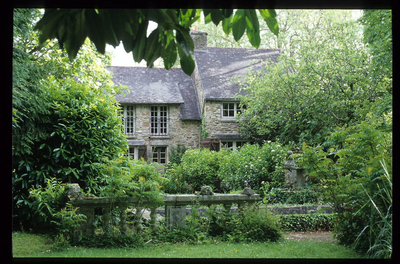 A stone building surrounded by green foliage on Jean Royère's estate in Brittany