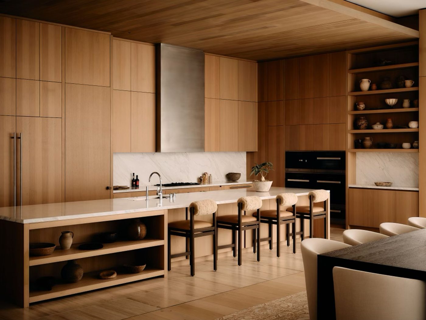 Kitchen area of penthouse in Los Angeles West Hollywood designed by Adair Lewis of JSN Studio with natural wood fnished cabinets, shearling backed barstools, black appliances