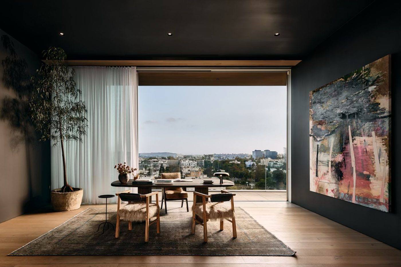Home office in penthouse in Los Angeles West Hollywood designed by Adair Lewis of JSN Studio with Pierre Jeanneret and goat-hair-covered chairs and dark wood table desk in front of wall of glass that opens to balcony