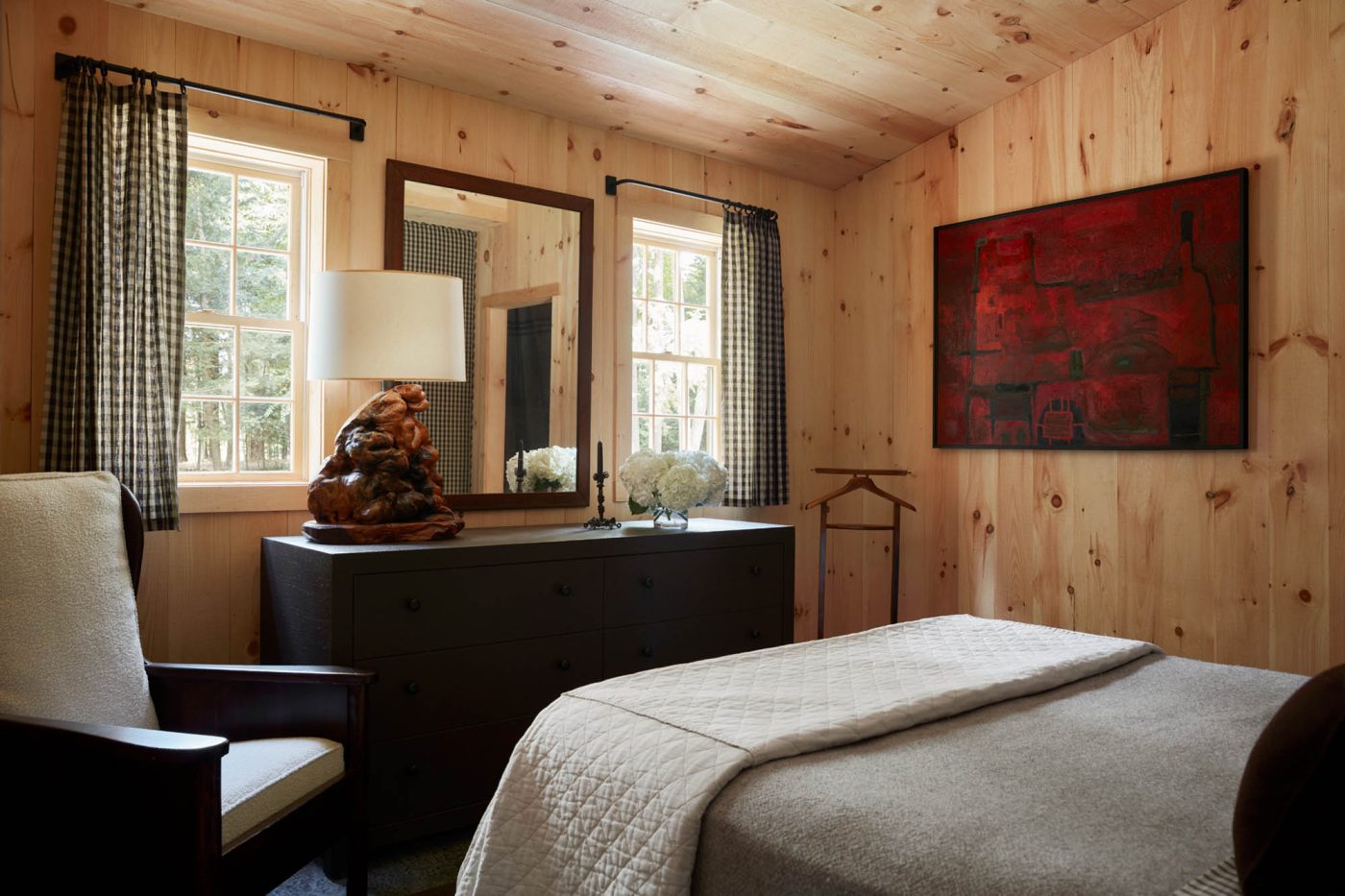 To one side of the bed sits an English-style painted-pine wing chair with custom cushions and, to the other, a mid-century valet by Ico Parisi for Fratelli Reguitti . Hanging on the wall is a deep carmine painting by Svetozar Radakovich