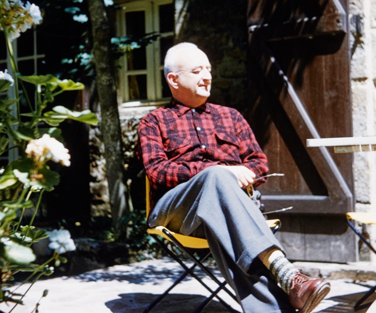 Jean Royère wearing a red plaid shirt and sitting in a yellow folding chair in the garden of his home in Brittany