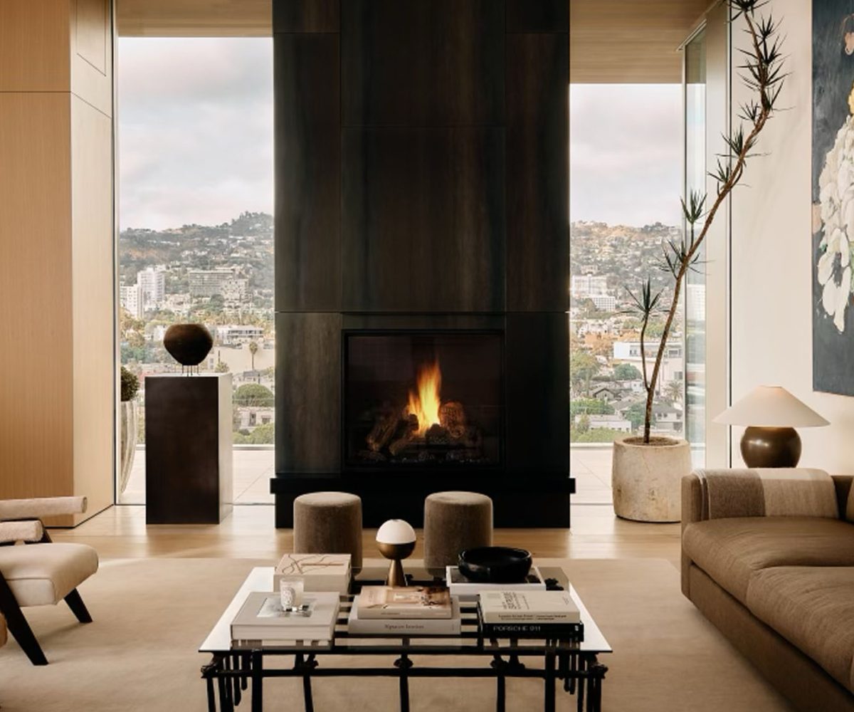 Living area in front of fireplace in penthouse in Los Angeles West Hollywood designed by Adair Lewis of JSN Studio furnished with Pierre Jeanneret lounge chairs, an invory huted custom sofa, Pierre Frey–upholstered poufs, lamps from Studio Balestra and a coffee table
