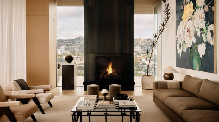 Living area in front of fireplace in penthouse in Los Angeles West Hollywood designed by Adair Lewis of JSN Studio furnished with Pierre Jeanneret lounge chairs, an invory huted custom sofa, Pierre Frey–upholstered poufs, lamps from Studio Balestra and a coffee table