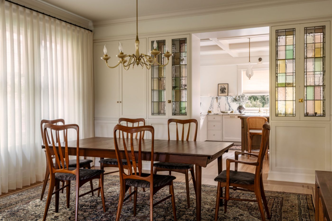 Dining room with mid-century-modern teak table and chairs and Murano glass chandelier above in a house in Seattle's Capitol Hill neighborhood designed by Lisa Staton. View to kitchen through stain-glass-fronted cabinets