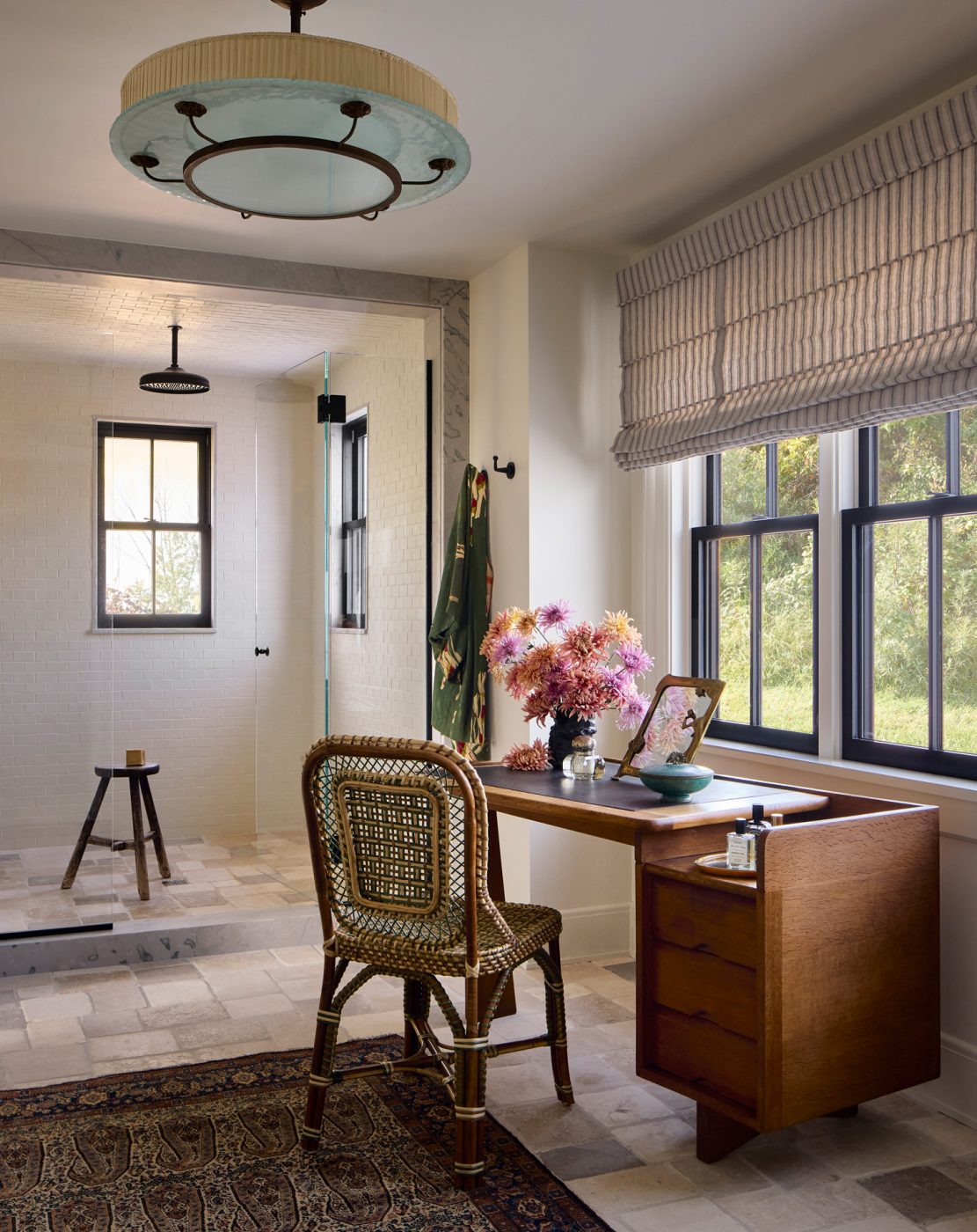 The primary bathroom features a vintage Guillerme & Chambron vanity table from MORENTZ,met by a Marshan rattan side chair by Creel and Gow. A Swedish vintage light fixture