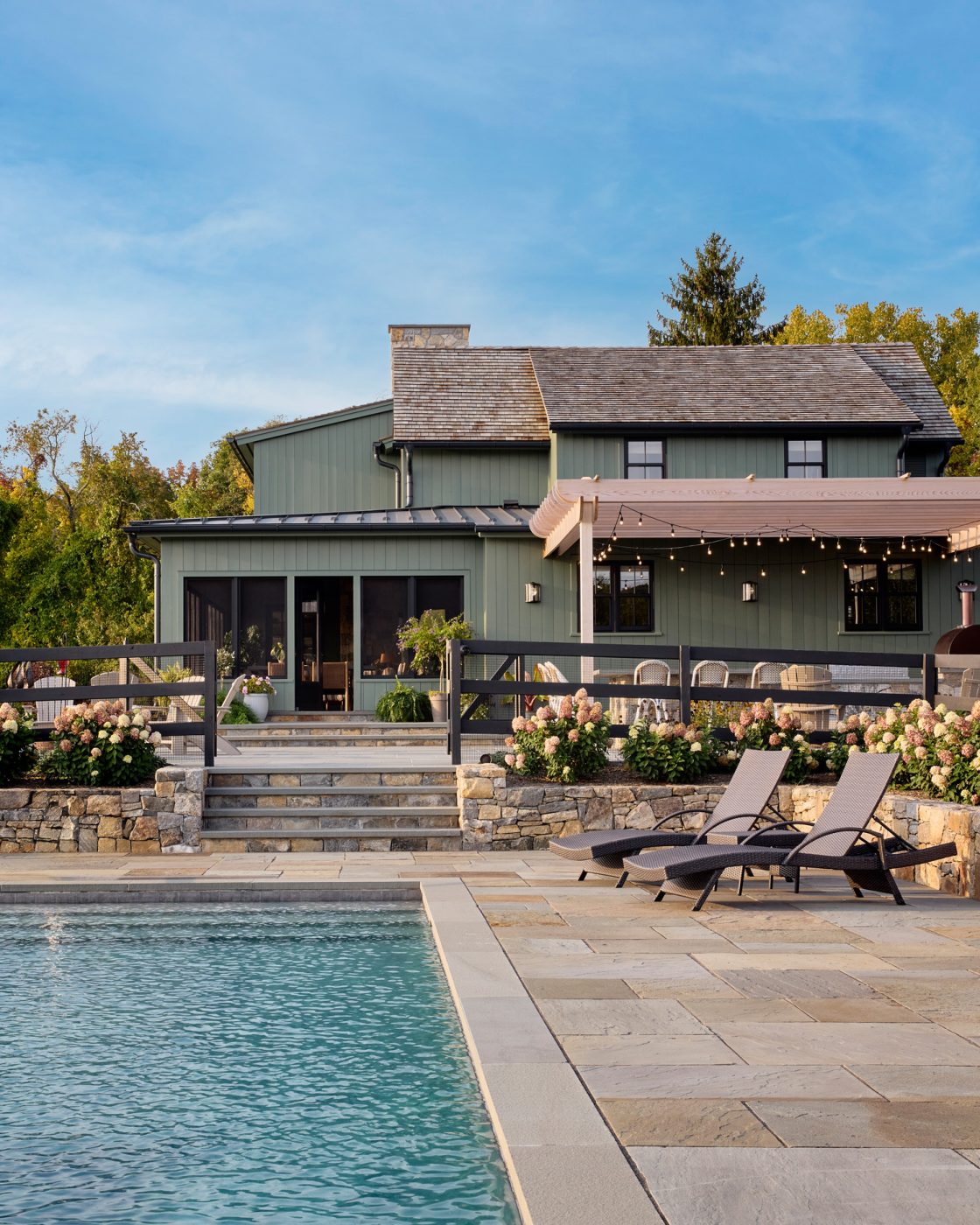 Behind the pool, a pergola shelters the outdoor bar and barbecue pit, making the space ideal for gatherings.