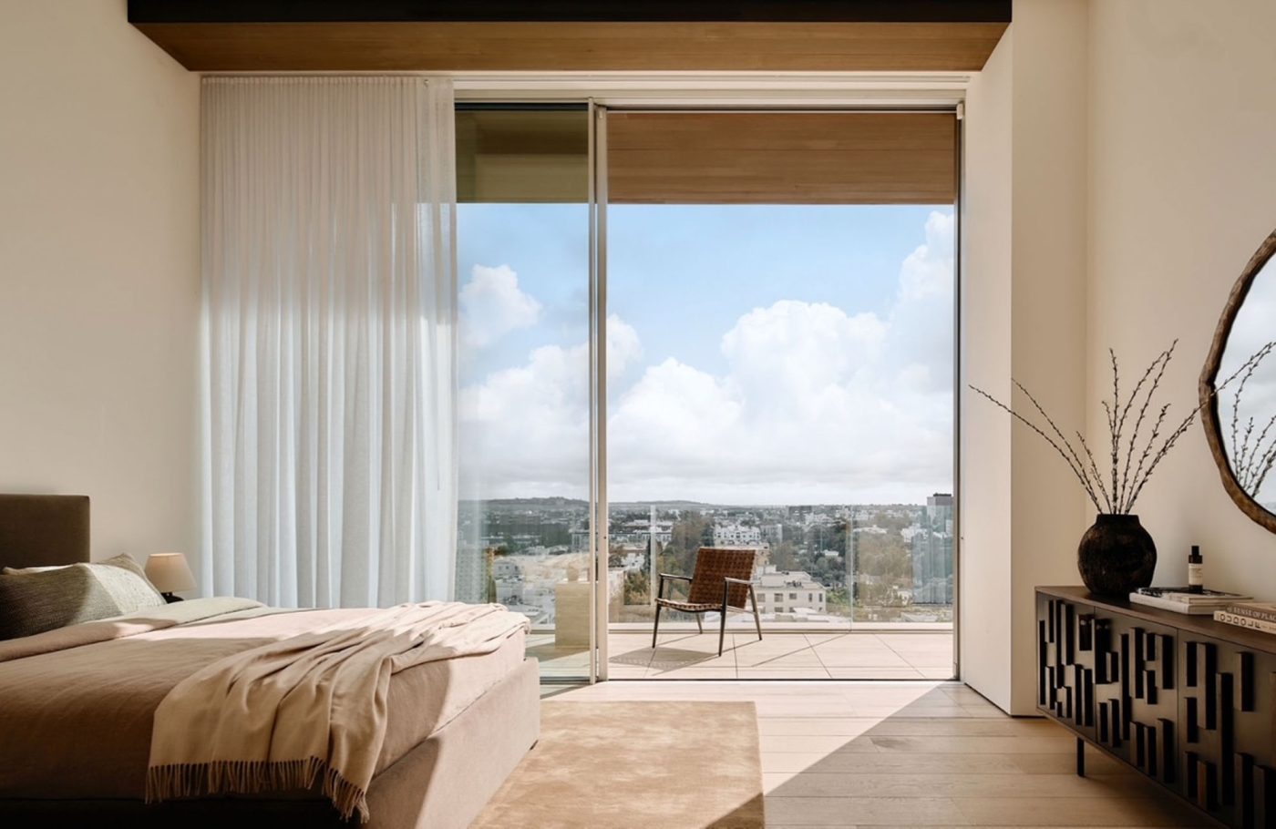 Primary bedroom in penthouse in Los Angeles West Hollywood designed by Adair Lewis of JSN Studio furnished  with upholstered, textured credenza. opend to balcony through sliding wall of glass 