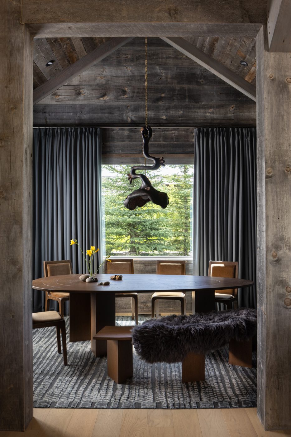 Roman and Williams Guild’s Stockholm Coupe velvet dining chairs and a Vincent Poscik pendant over an oblong table in the rustic wood-paneled dining room of a ranch house with interiors designed by Valerie Peña in Jackson Hole Wyoming