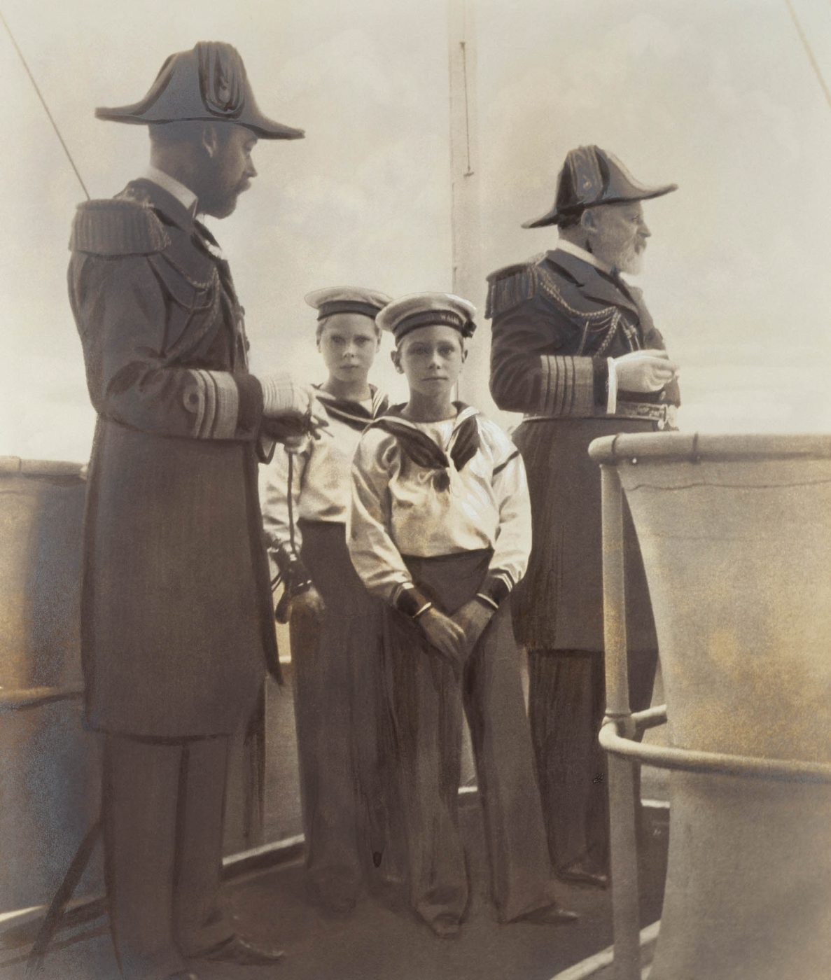 A black and white photo of George, Prince of Wales (later King George V), with his sons Prince Edward (King Edward VIII) and Prince Albert (King George VI) and his father, King Edward VII, in naval dress